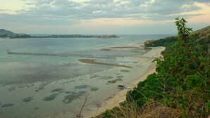 A coastal landscape with a beach, a pier, and distant islands. - Puri Komodo Resort (Labuan Bajo)