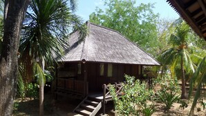 A wooden house with a thatched roof, surrounded by palm trees and a paved area with steps leading to the entrance. - Puri Komodo Resort (Labuan Bajo)