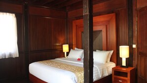 A wooden four-poster bed with white linens and a decorative headboard. There are two bedside tables with lamps. - Puri Komodo Resort (Labuan Bajo)