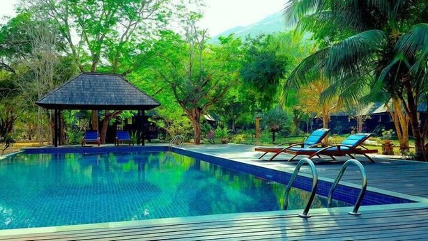 A swimming pool with lounge chairs and a gazebo surrounded by lush greenery. - Puri Komodo Resort (Labuan Bajo)