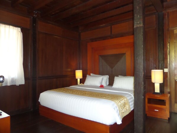 A wooden-framed bedroom with a large bed, two bedside tables, and a window with curtains. - Puri Komodo Resort (Labuan Bajo)
