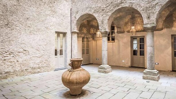 Un patio interior con paredes de piedra, arcos y un jarrón grande.
