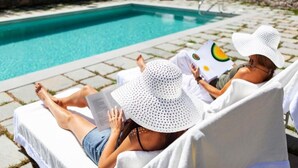 Dos personas descansando junto a una silla de piscina, leyendo un libro.