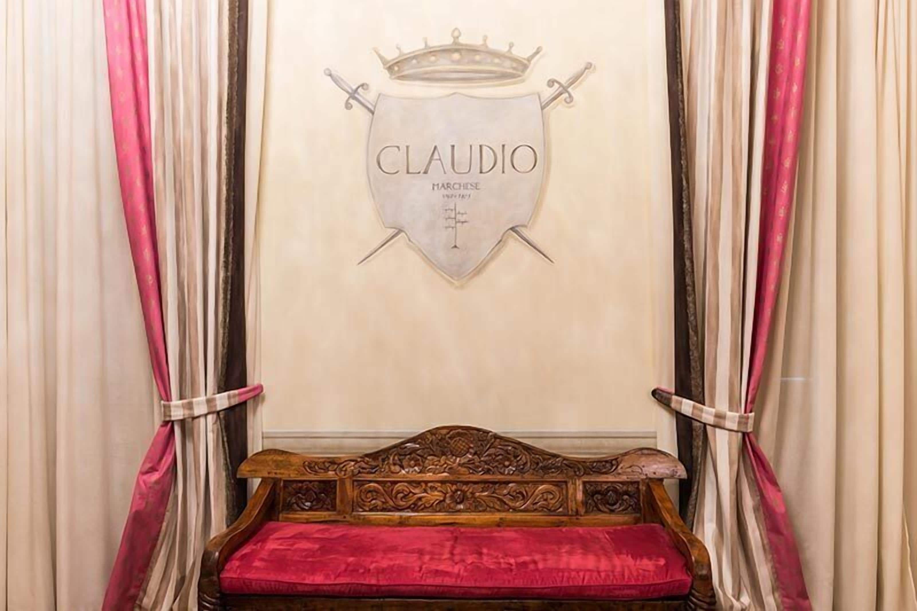 Une pièce comprenant un lit, un écusson fixé au mur portant le nom « CLAUDIO », et des rideaux.