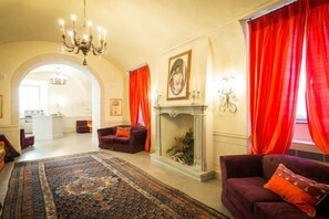 A spacious living room with a fireplace, red curtains, and a chandelier. - Castello di Pontebosio Luxury Resort (Licciana Nardi)