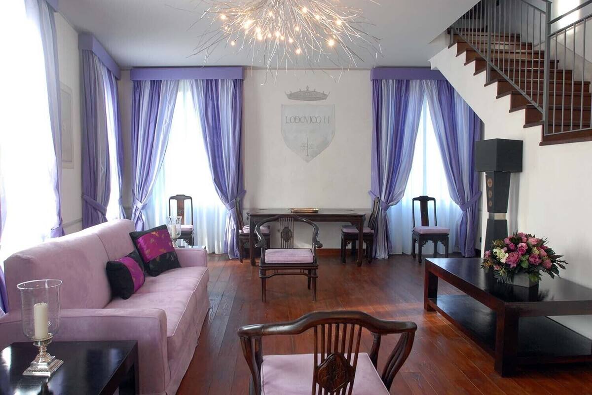 Una sala de estar con sofá rosa, sillas de madera, chimenea y una escalera.