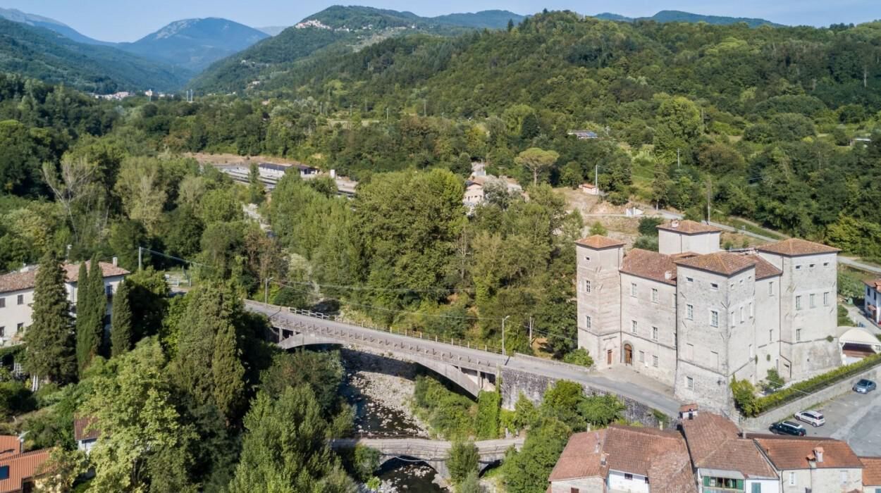 Un pueblo rural con un puente de piedra, edificios tradicionales y abundante vegetación.