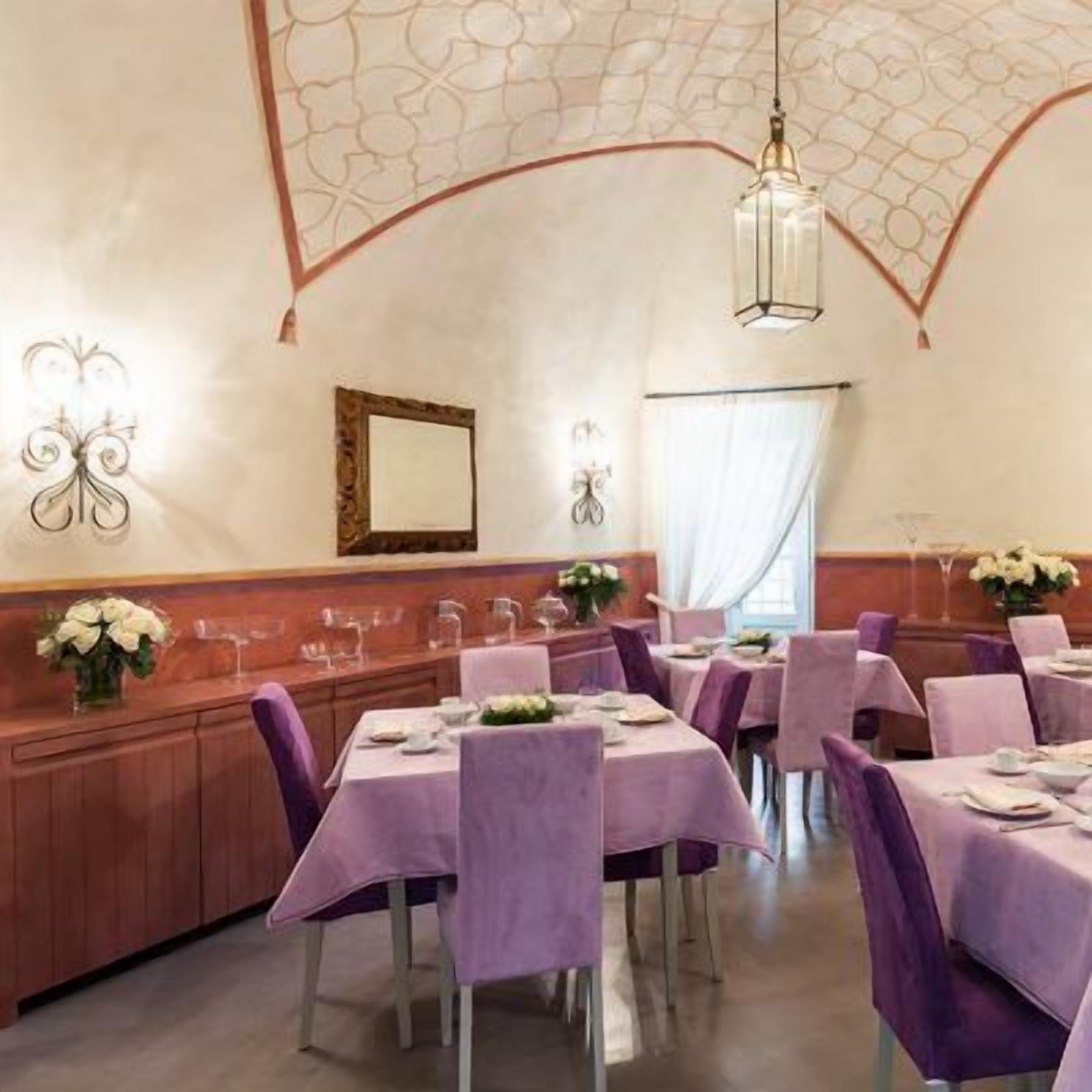 Zona pranzo con tavoli apparecchiati, soffitto decorativo e lampade a parete.