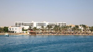 A coastal hotel with multiple floors, a beach in the background, and palm trees.