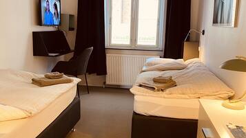A hotel room with two beds, a desk, a chair, a TV, and a window with curtains.