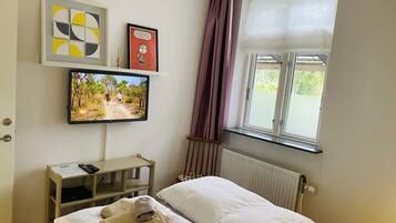 Makuuhuoneessa on sänky, seinälle asennettu televisio, ikkuna, jossa on verhot, ja patteri.