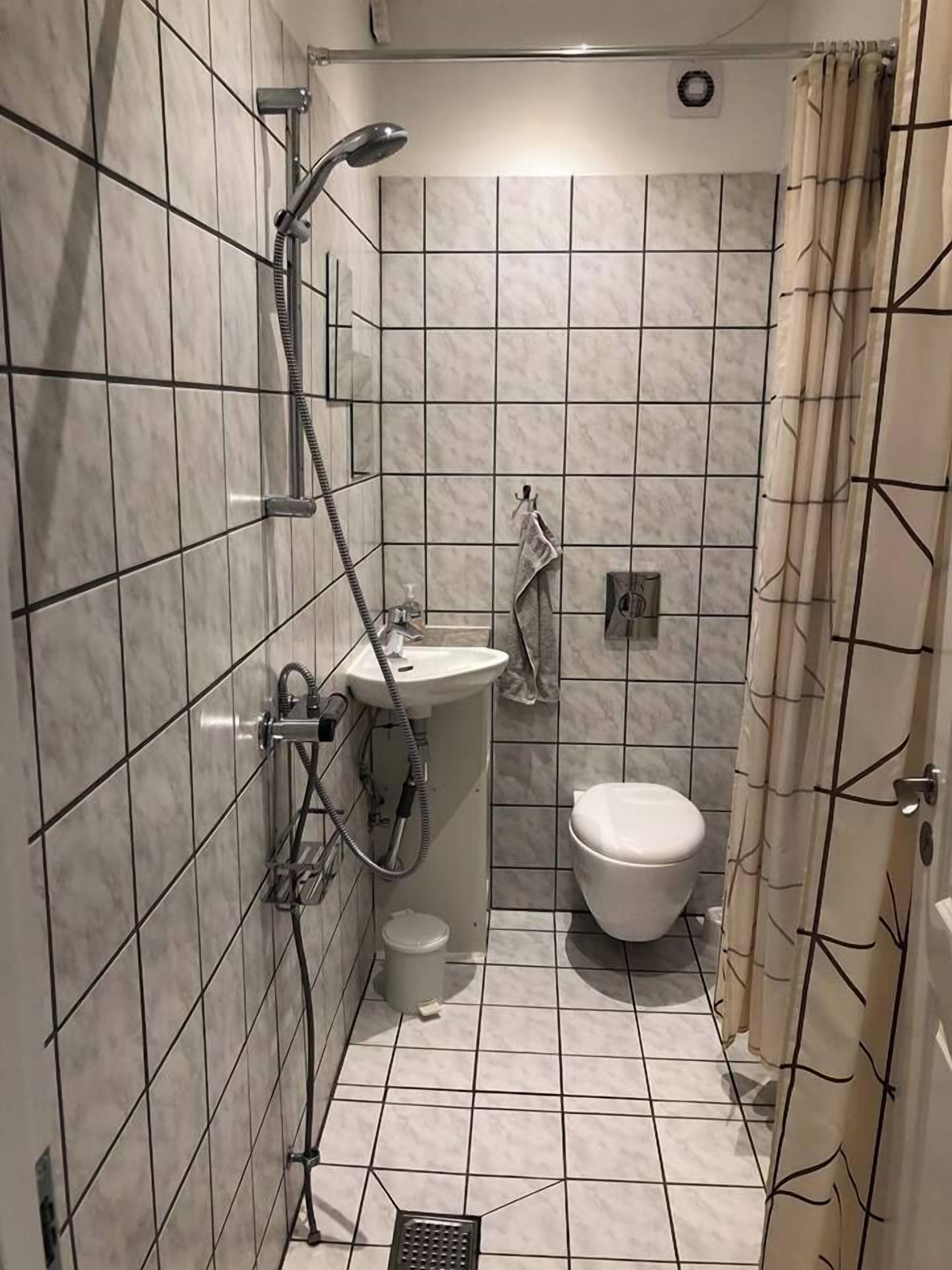 Ein kleines Badezimmer mit Fliesen, einer Dusche, einem Waschbecken und einer Toilette.