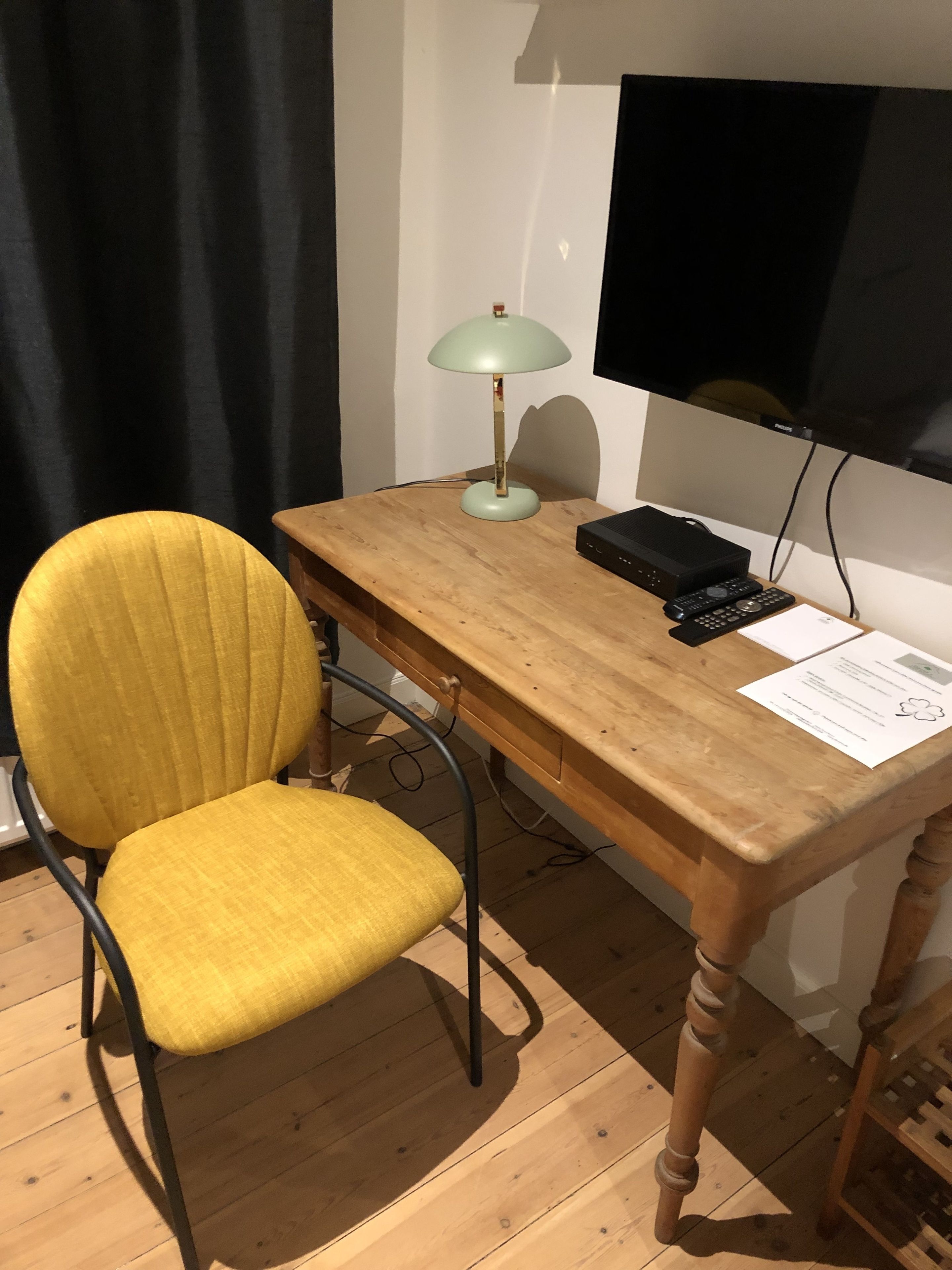 A wooden desk with a yellow chair, a lamp, a television, and a remote control.