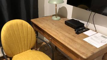 A wooden desk with a yellow chair, a lamp, a television, and a remote control.