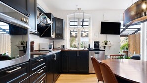 A modern kitchen with dark cabinetry, a wooden dining table, and a built-in oven. - Davaa’S Bed and Breakfast (Randers)