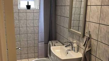 Un baño con inodoro, lavamanos y ventana con cortina.
