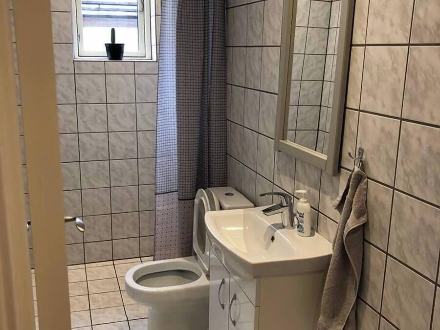 Un baño con inodoro, lavamanos y ventana con cortina.