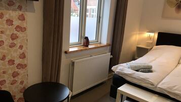 A hotel room with a bed, bedside table, window, radiator, and a small table.