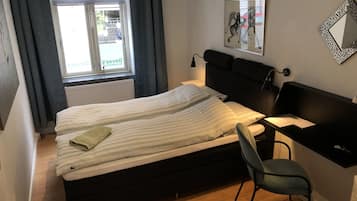 Una camera da letto con un letto, una scrivania, una sedia, un termosifone, una finestra con tende e uno specchio fissato al muro.