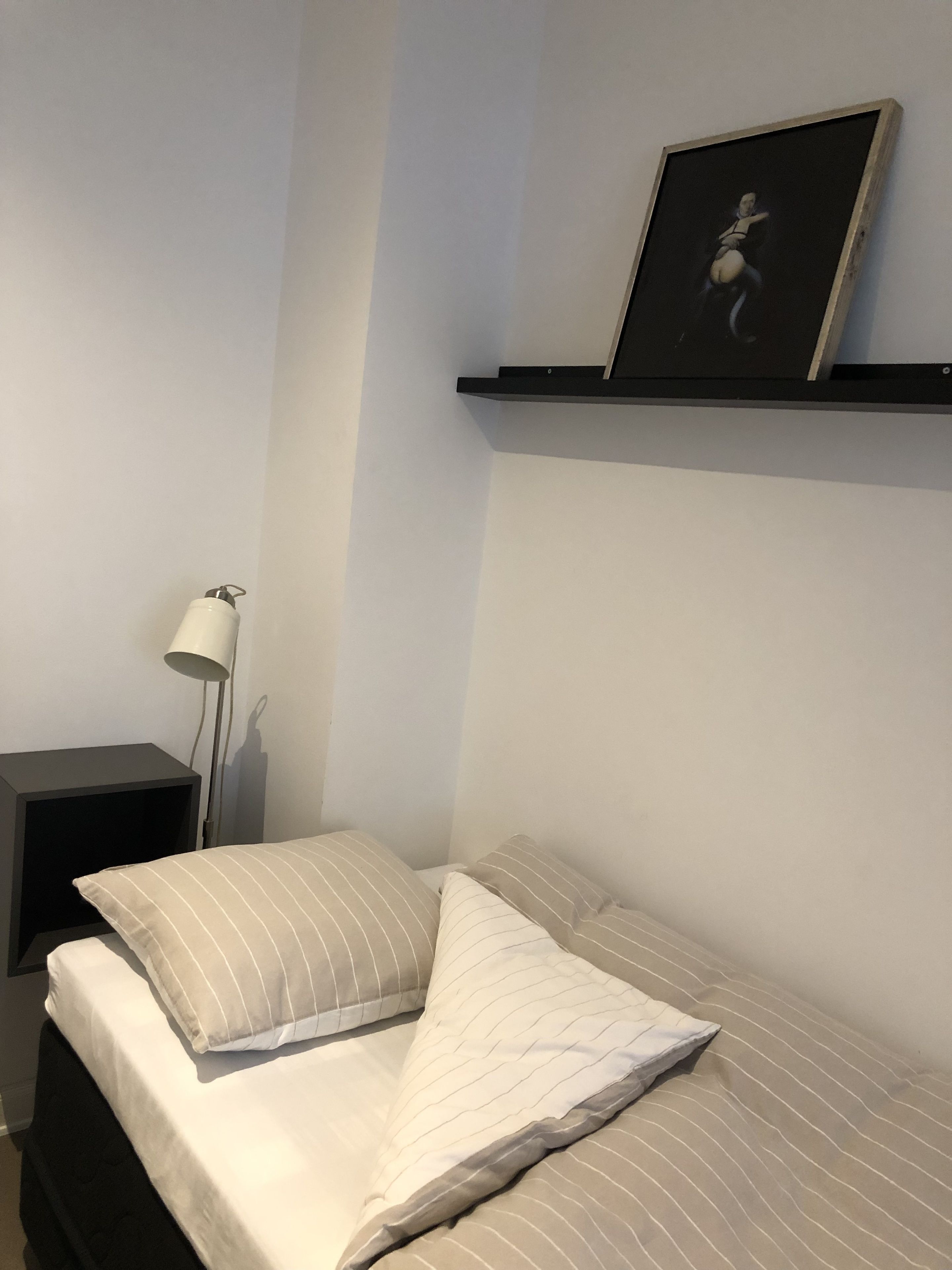 A bedroom with a bed, a nightstand, a lamp, and a framed picture on the wall.