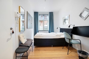 A bedroom with a bed, a desk, a chair, a window with curtains, a mirror, and a wall-mounted shelf. - Davaa’S Bed and Breakfast (Randers)