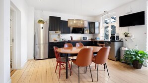 A modern kitchen with a dining area, featuring a large wooden table, red chairs, and stainless steel appliances. - Davaa’S Bed and Breakfast (Randers)