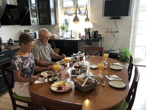 A dining area with a round table, chairs, and a variety of breakfast items including bread, fruit, and beverages. - Davaa’S Bed and Breakfast (Randers)