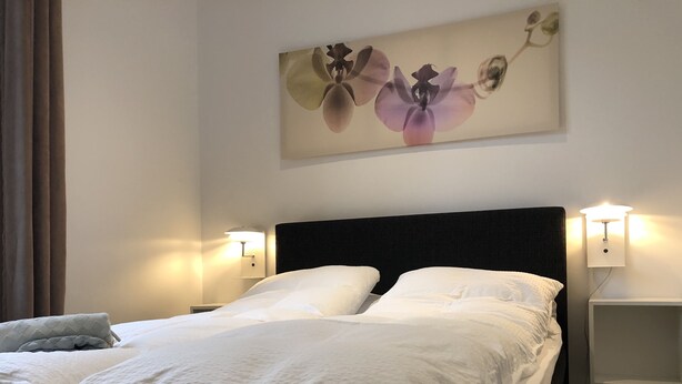 A neatly made bed with white linens, a dark headboard, and two bedside lamps. - Davaa’S Bed and Breakfast (Randers)