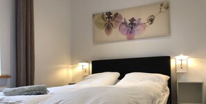 Un lit bien fait, avec du linge de lit blanc, une tête de lit sombre et deux lampes de chevet.
