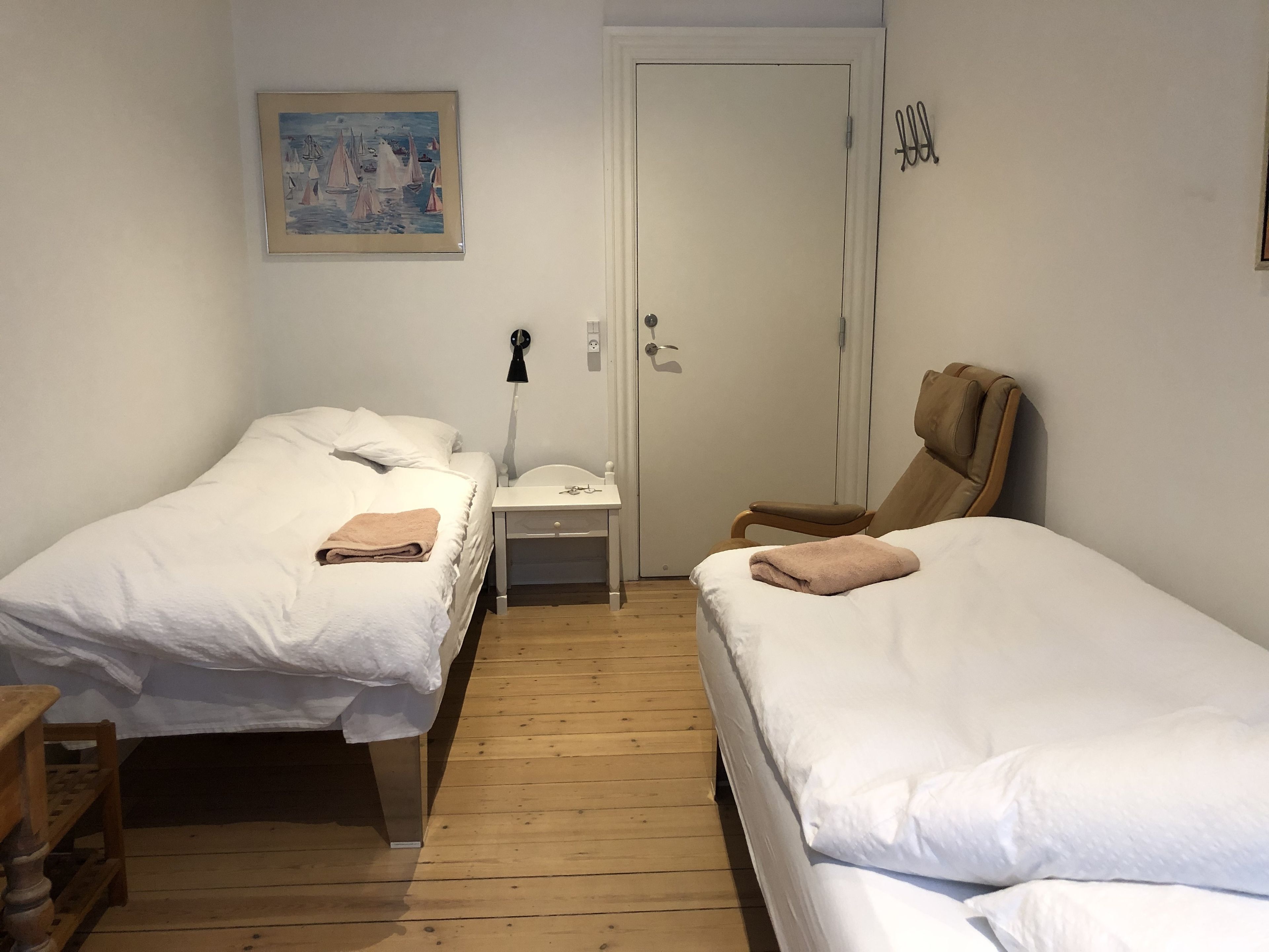 Una habitación con dos camas, una mesita, una silla y una puerta.