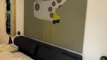 Et hotelværelse med en seng, et natbord med en lampe, og et vægmaleri af et stiliseret dyr.