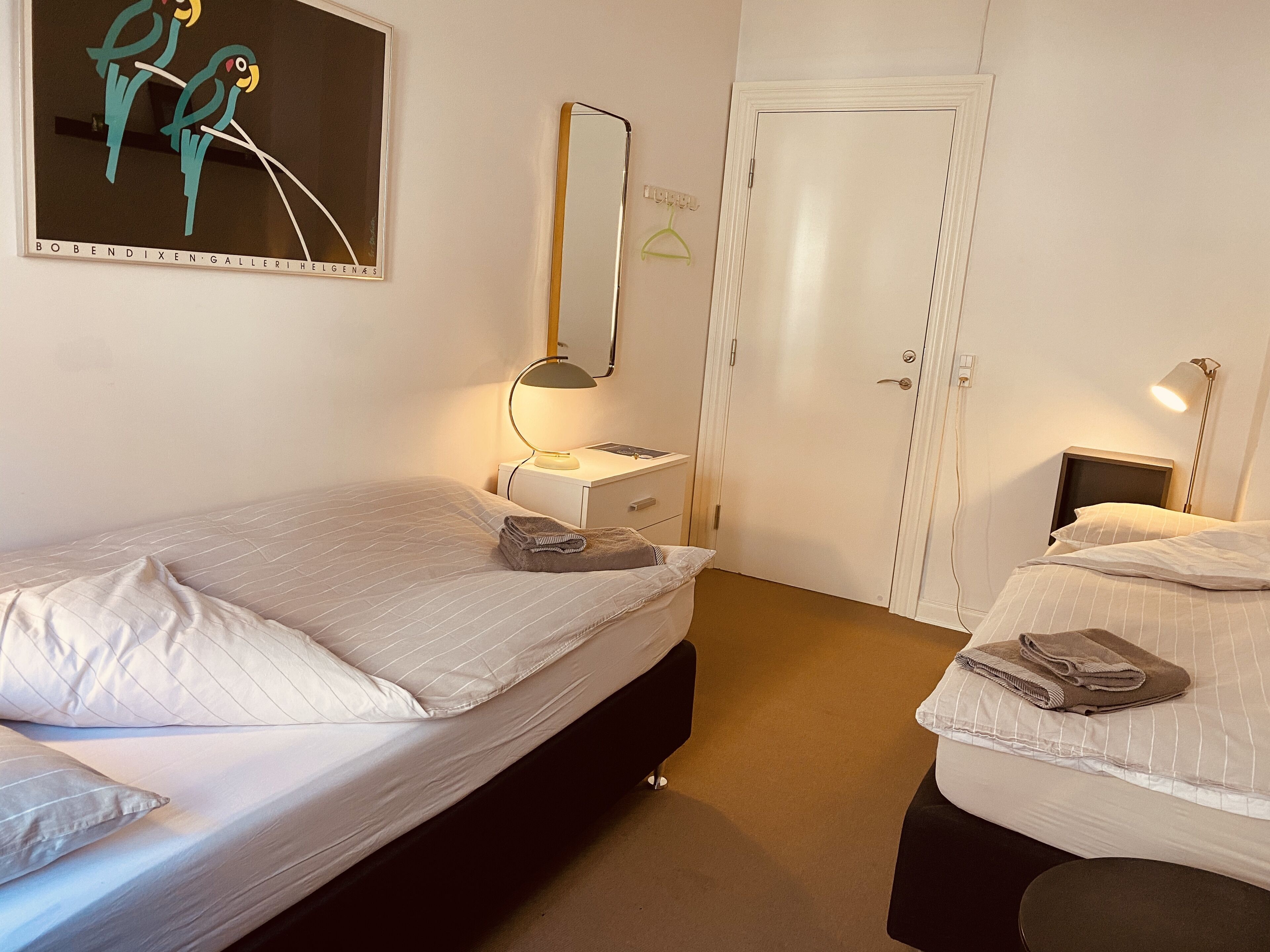 Habitación de hotel con dos camas, un escritorio, una silla, una lámpara y un cuadro en la pared.