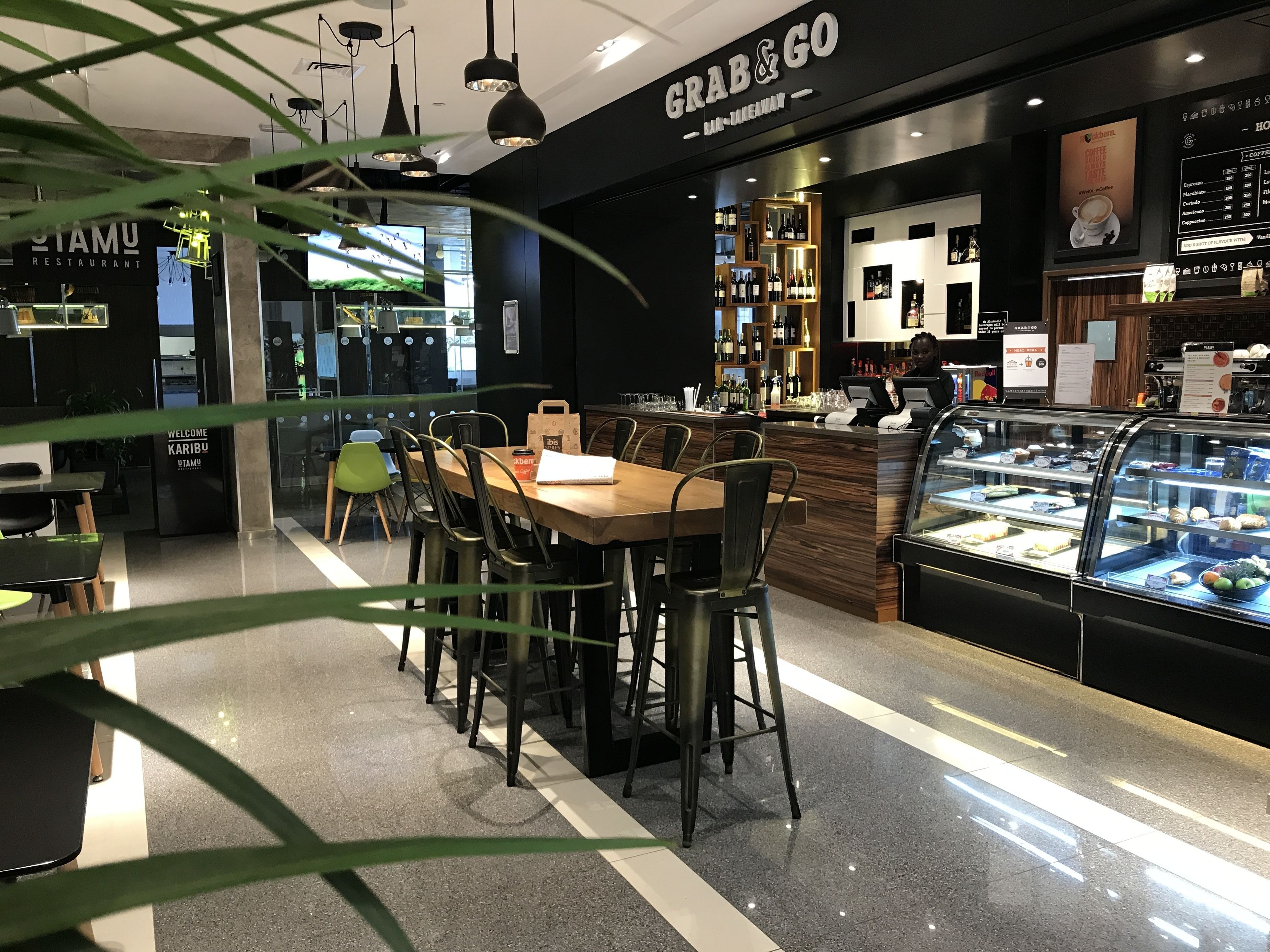 Interior de una cafetería moderna con una mesa y sillas de madera, una barra con vitrina y una pizarra de menú.