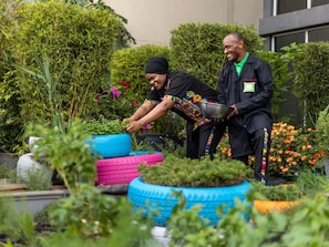 Two individuals gardening in a lush, green outdoor area with various plants and colorful tire planters. - ibis Styles Nairobi Westlands (Nairobi)