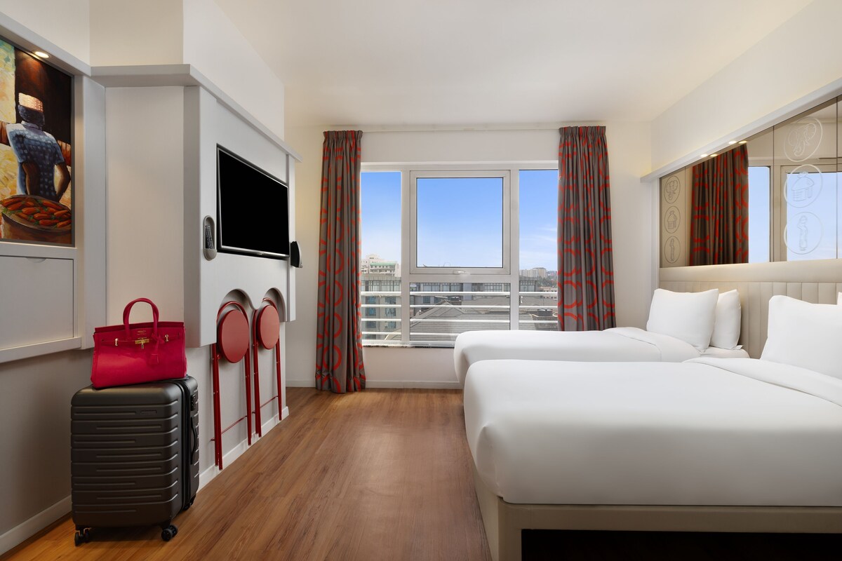 Habitación de hotel con cama, escritorio, televisor, maleta y un cuadro en la pared.