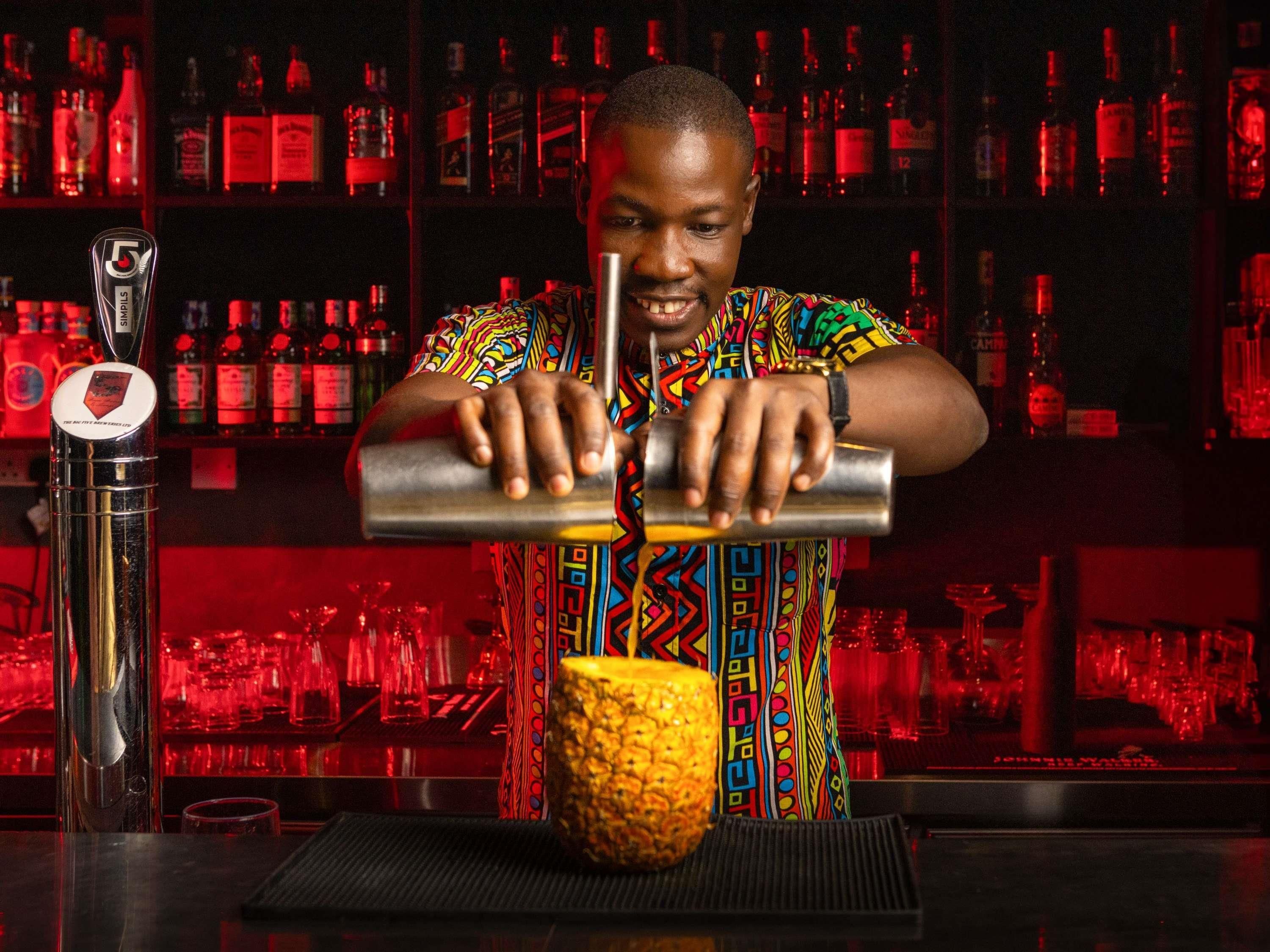 A bartender preparing a drink with a shaker and a pineapple on the counter.