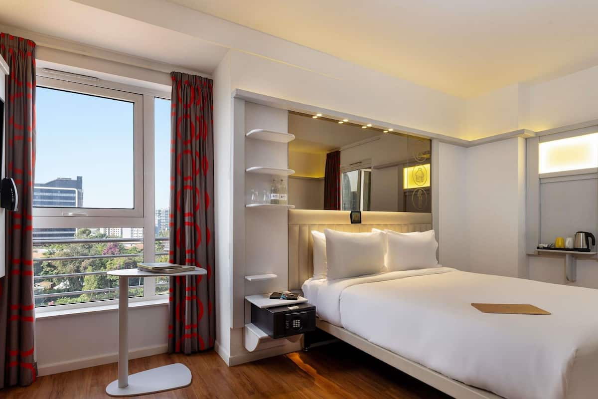 Hotelkamer met een groot bed, nachtkastjes, een klein rond tafeltje, een magnetron en uitzicht op de stad.