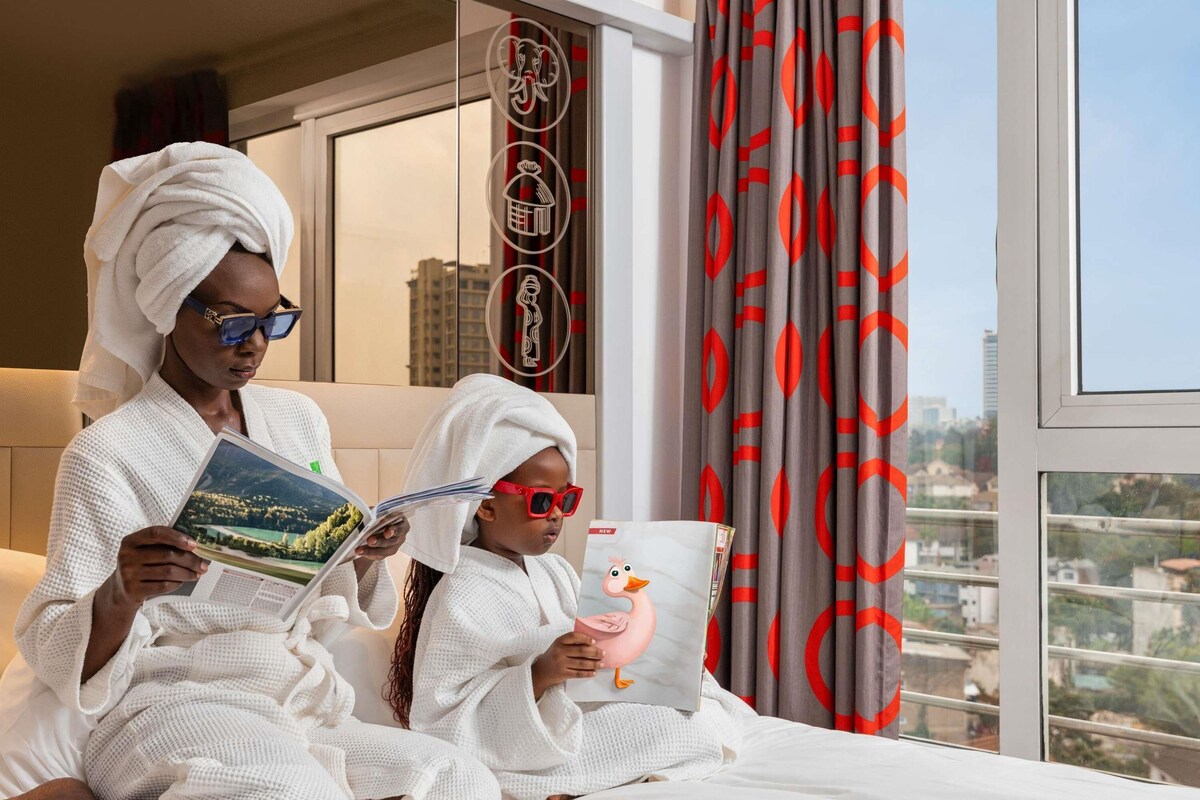 Dos personas vestidas de blanco sentadas en una cama leyendo libros, con vistas a la ciudad.