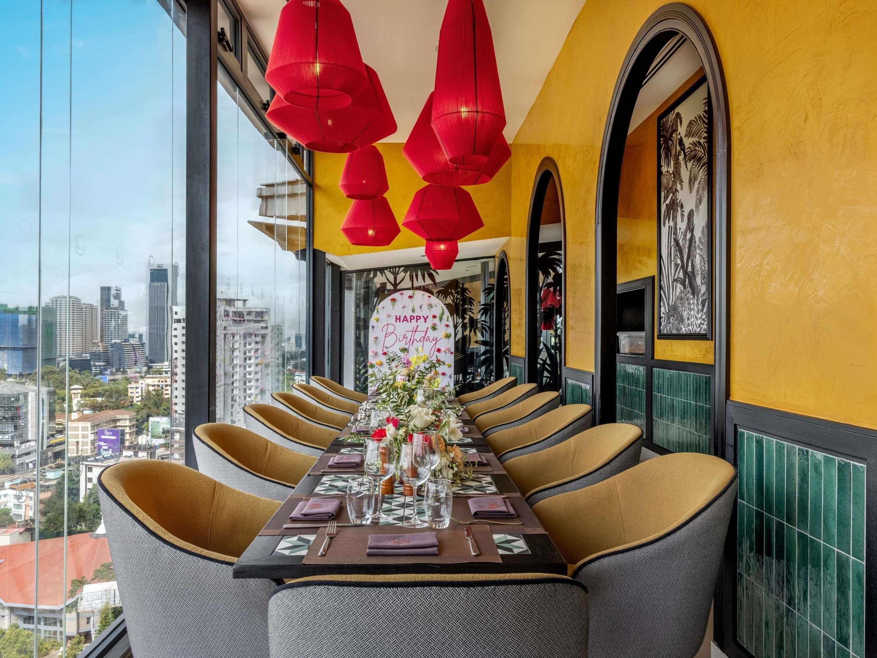A dining area with a city view, a table set for four, and red hanging lights.
