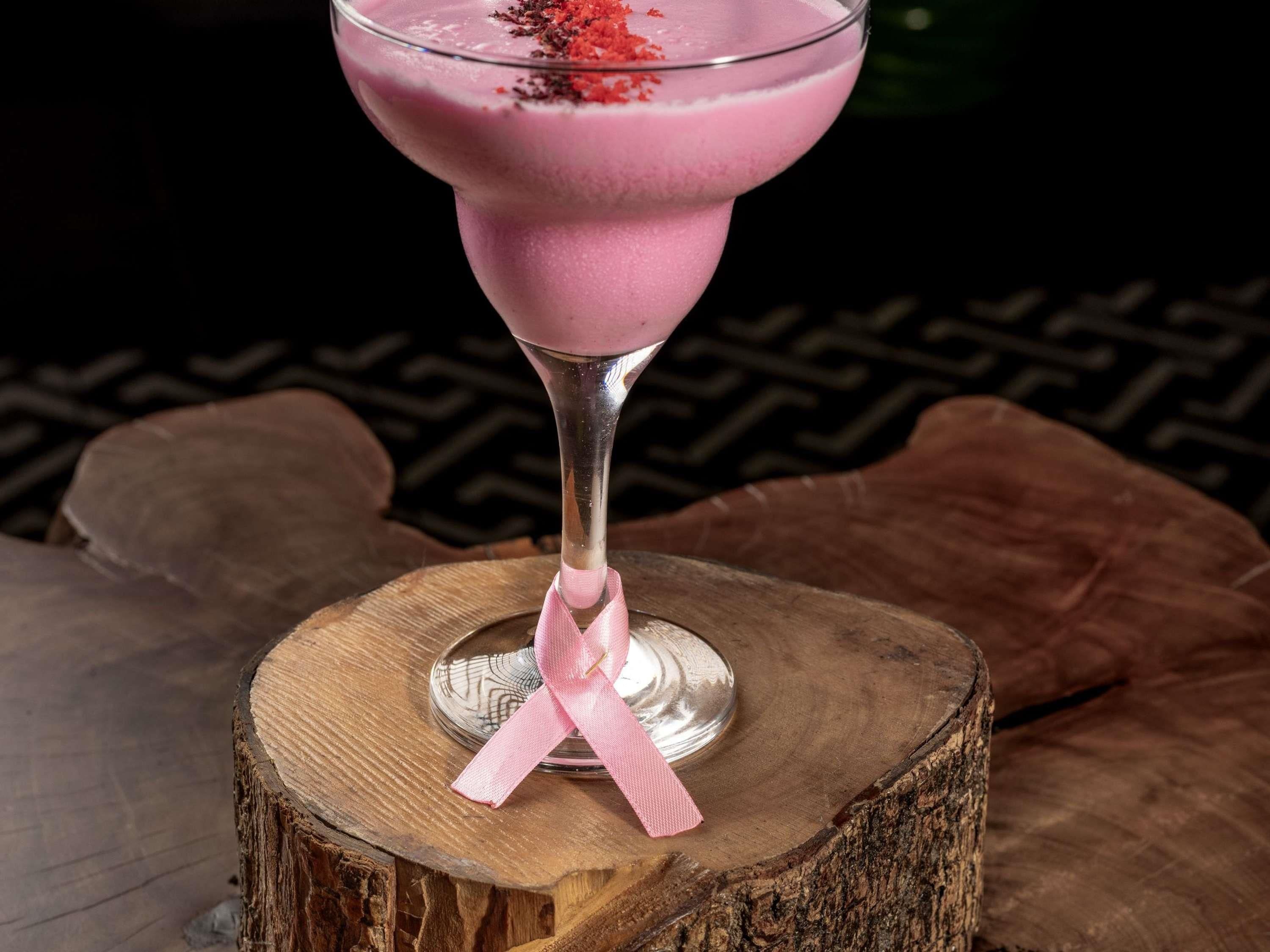A pink cocktail in a glass with a pink ribbon, placed on a wooden stump.
