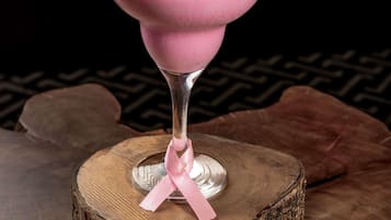 Un cóctel rosado en un vaso con un lazo rosa, sobre un tocón de madera.