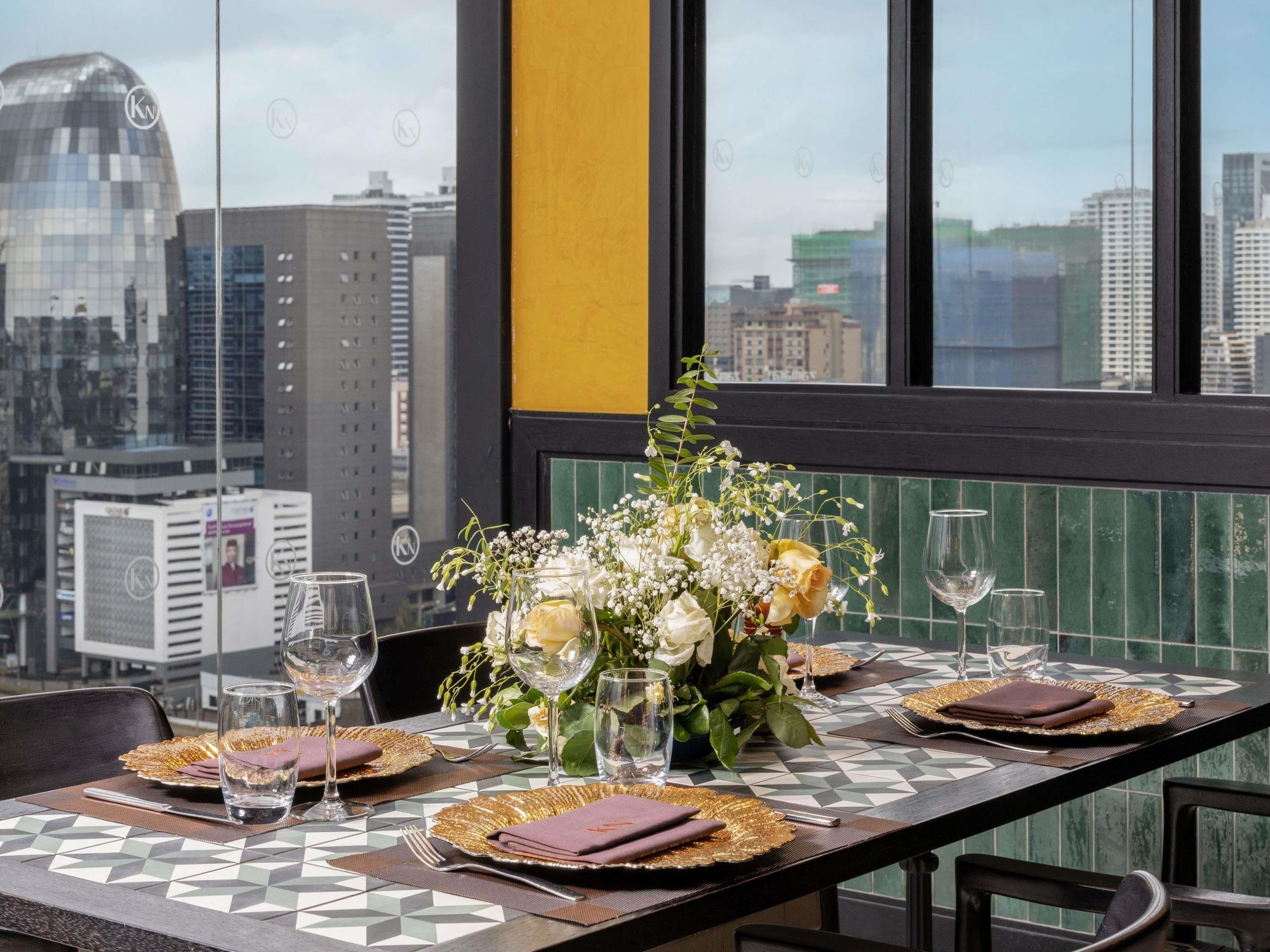 A dining table set with a view of a cityscape through large windows.