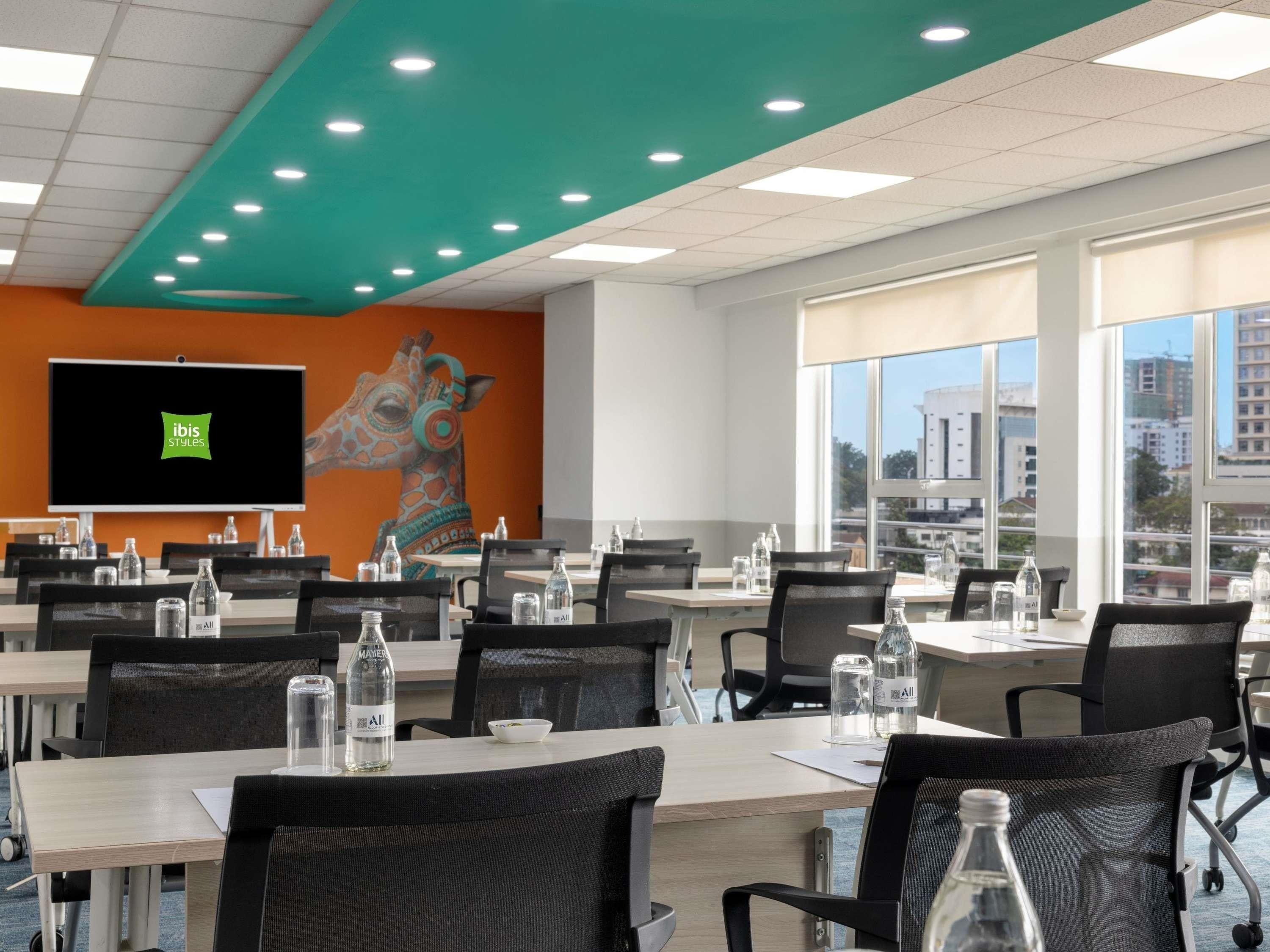 A conference room with tables, chairs, and a large screen.