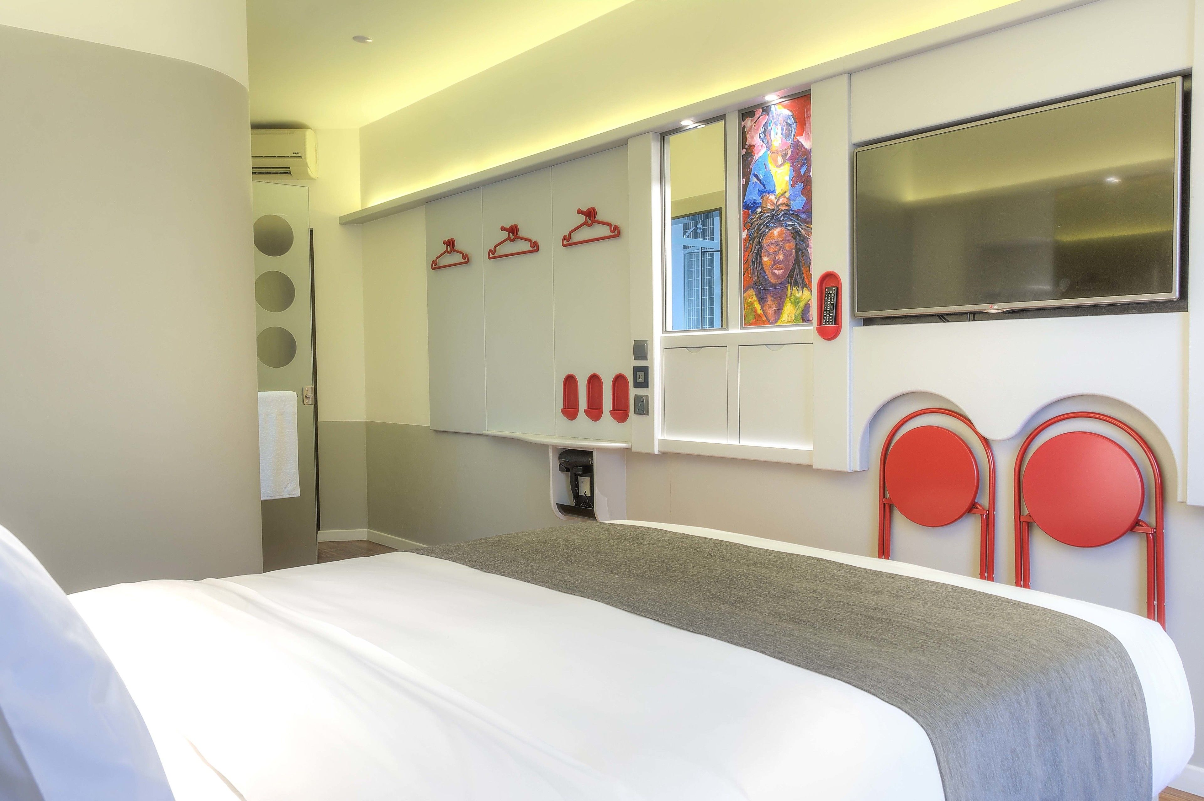 A hotel room with a bed, a large mirror, a flat-screen TV, and a wardrobe with circular mirrors and red hangers.