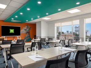 Une salle de conférence dotée d’un grand écran affichant le logo « ibis Styles », d’une fresque représentant une girafe et offrant une vue sur la ville grâce à de grandes fenêtres.