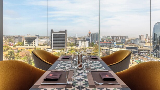A dining table with chairs, a city view, and a table setting with glasses and cutlery.