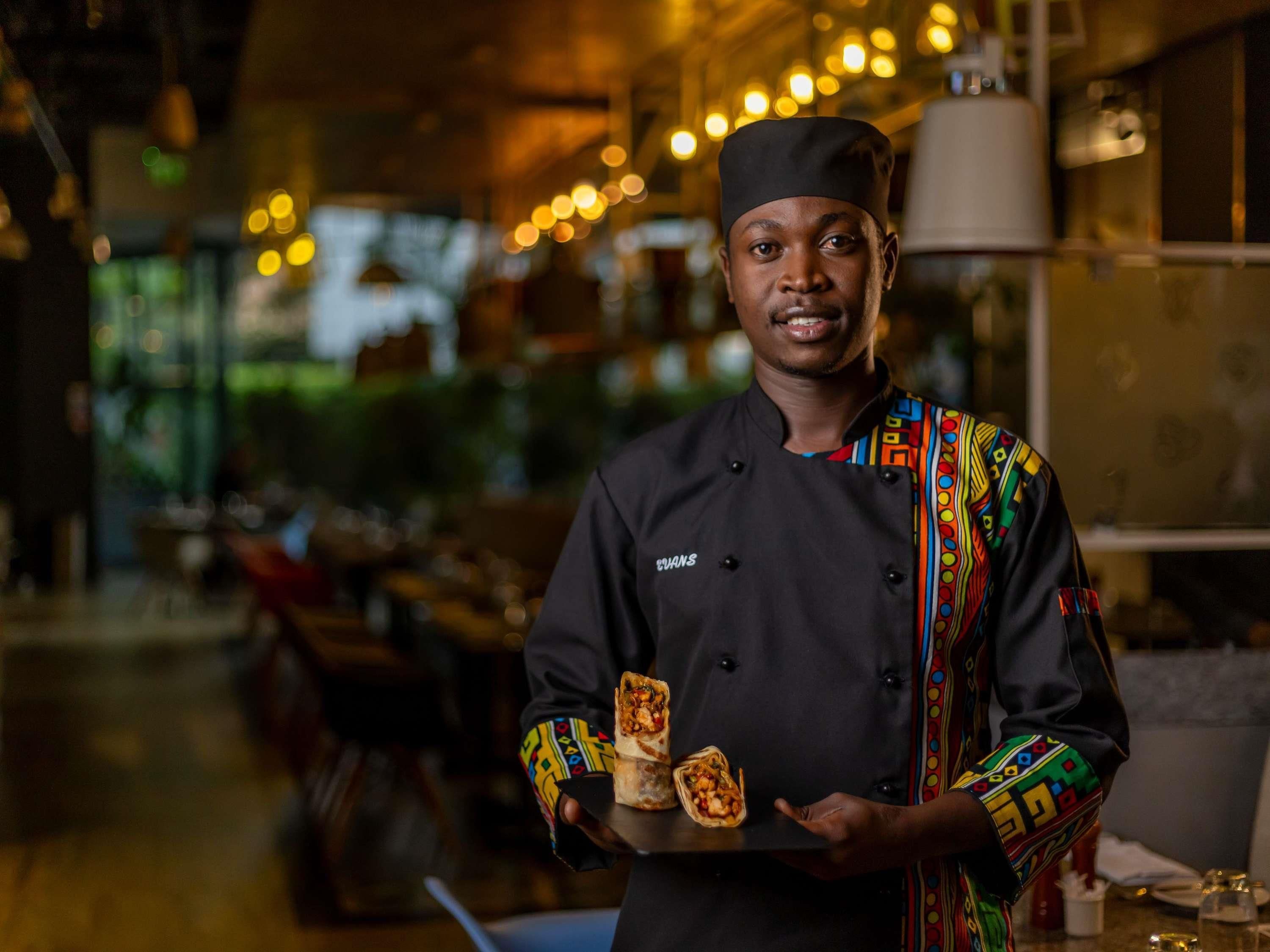 A chef holding a tray with food items in a restaurant setting.