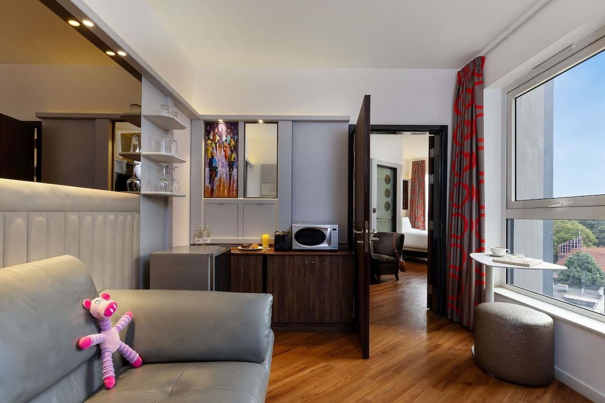 Una habitación de hotel moderna con sofá, una mesita, microondas, armario y ventana con vistas.