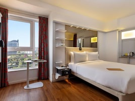 Habitación de hotel con una cama grande, mesitas de noche, una pequeña mesa redonda, un microondas y una ventana con cortinas.