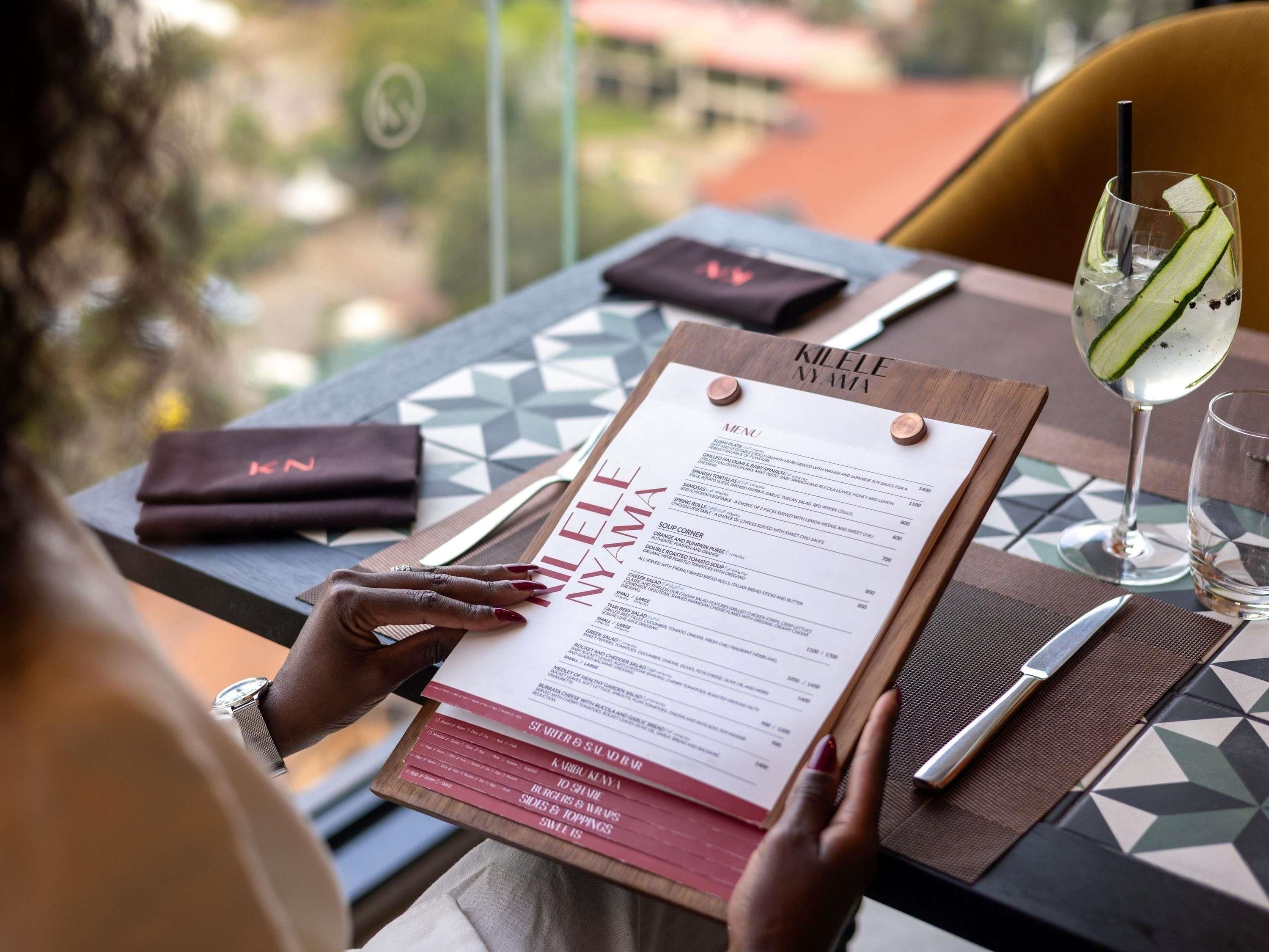 Une personne est assise à une table, tenant un menu, avec une boisson et une serviette à proximité.